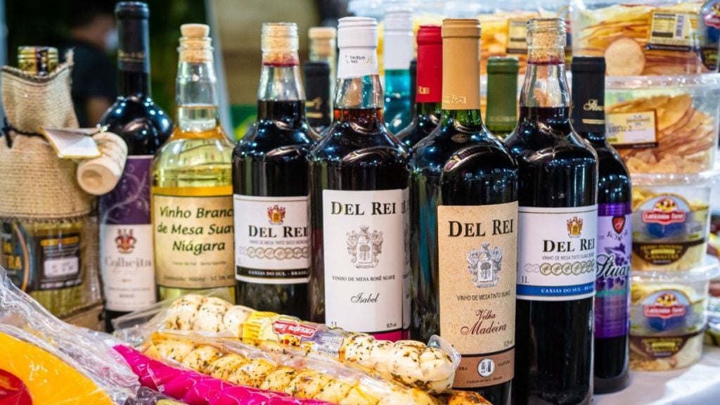 Mesa de produtos e bebidas artesanais em feira: garrafas de vinho e alimentos embalados, destacando a culinária do Sul na ExpoGaúcha em Santos.