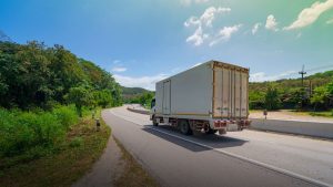 Caminhão de carga em rodovia cercada por vegetação, transportando contêiner; cenário que ilustra o frete rodoviário e mudanças aprovadas no Senado.
