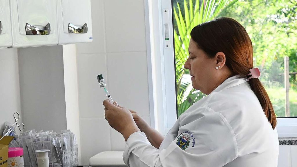 Profissional de saúde realiza preparo com seringa em laboratório, ao lado de materiais e vidrarias. Foto ilustrativa sobre mortes por gripe em Campinas, com aumento de óbitos