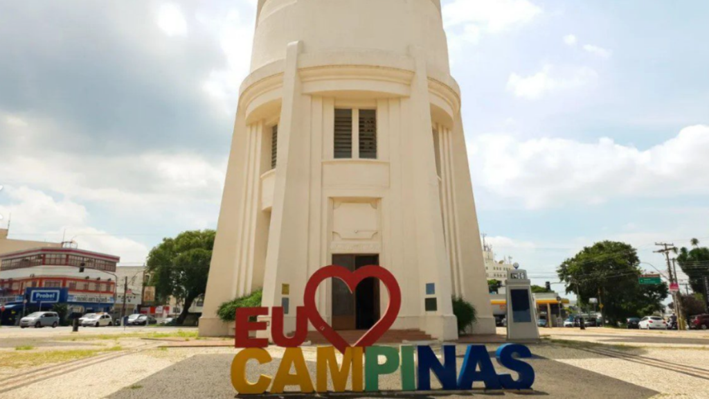 Monumento Eu Amo Campinas na entrada da cidade, com avenida ao fundo e veículos passando, destacando Campinas como polo de expansão urbana no mercado de loteamentos em SP.