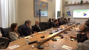 Reunião do Aviação Day em sala de conferências com autoridades e representantes do setor privado ao redor de uma mesa, equipamentos de áudio e telão com apresentação sobre o futuro da aviação brasileira.
