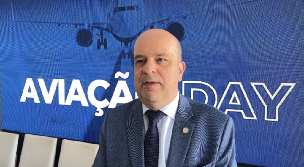 Adriano Miranda, superintendente de Serviços Aéreos da ANAC, em painel com o tema aviação day e imagem de aeronave ao fundo, em evento institucional.