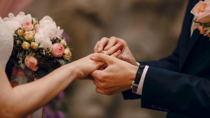 Casamento Comunitário em Santos: casal de mãos dadas com aliança trocada durante cerimônia, enquanto a noiva segura um buquê de flores. Informativo de adesão até 21 de agosto.