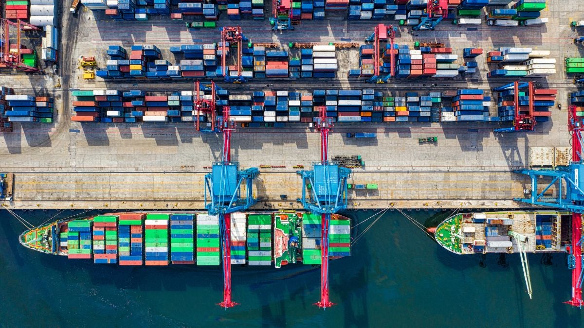 Vista aérea de um porto com navio porta-contêineres e diversos contêineres coloridos, cenário de transporte internacional relacionado ao tarifaço dos EUA e impacto em produtos brasileiros.