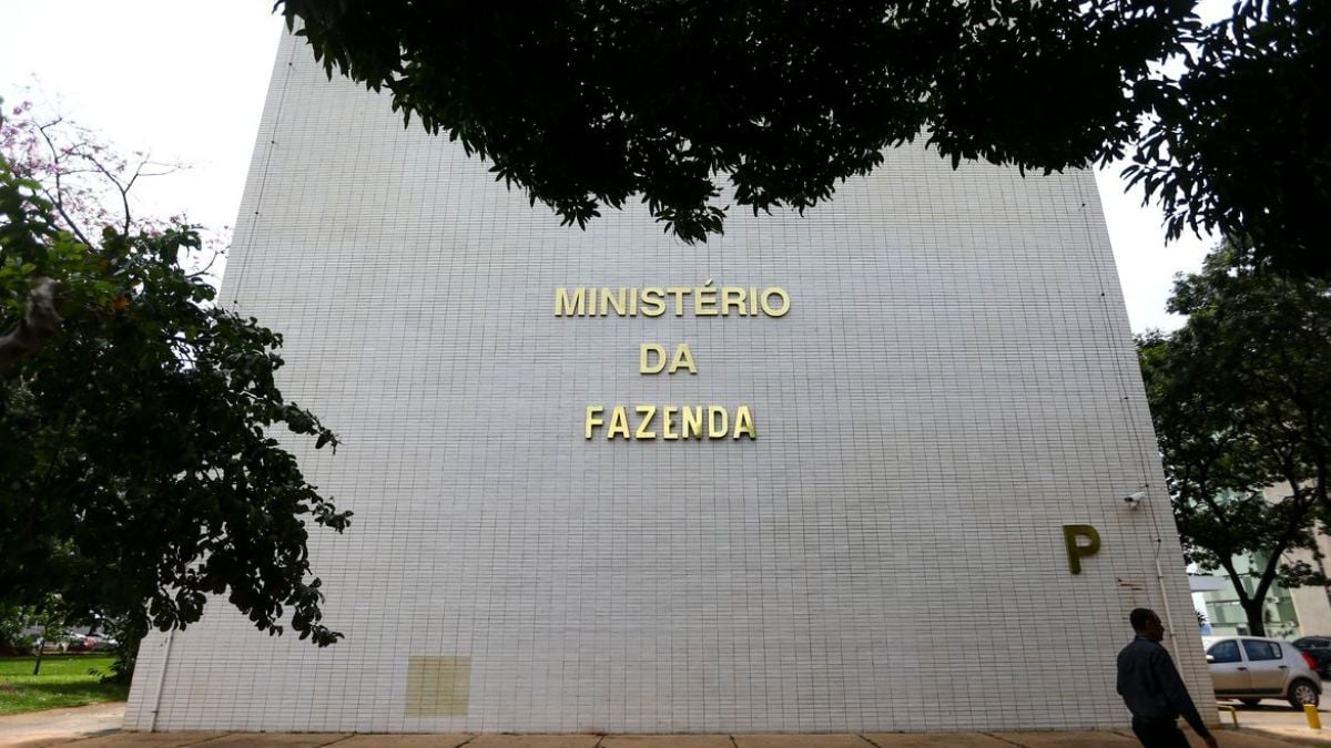 Prédio do Ministério da Fazenda ao ar livre, com árvores ao redor, destacando a fachada que informa “MINISTÉRIO DA FAZENDA”. Contexto ligado à inflação 2026, com governo elevando projeção para 5,1% e prevendo estouro da meta.