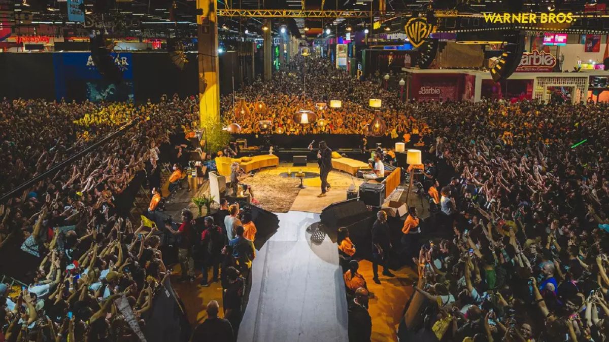 Vista de um grande palco durante a CCXP26, com multidão lotando o evento de cultura pop e banners de grandes marcas como Warner Bros e Barbie, ideal para divulgação de ingressos CCXP26.
