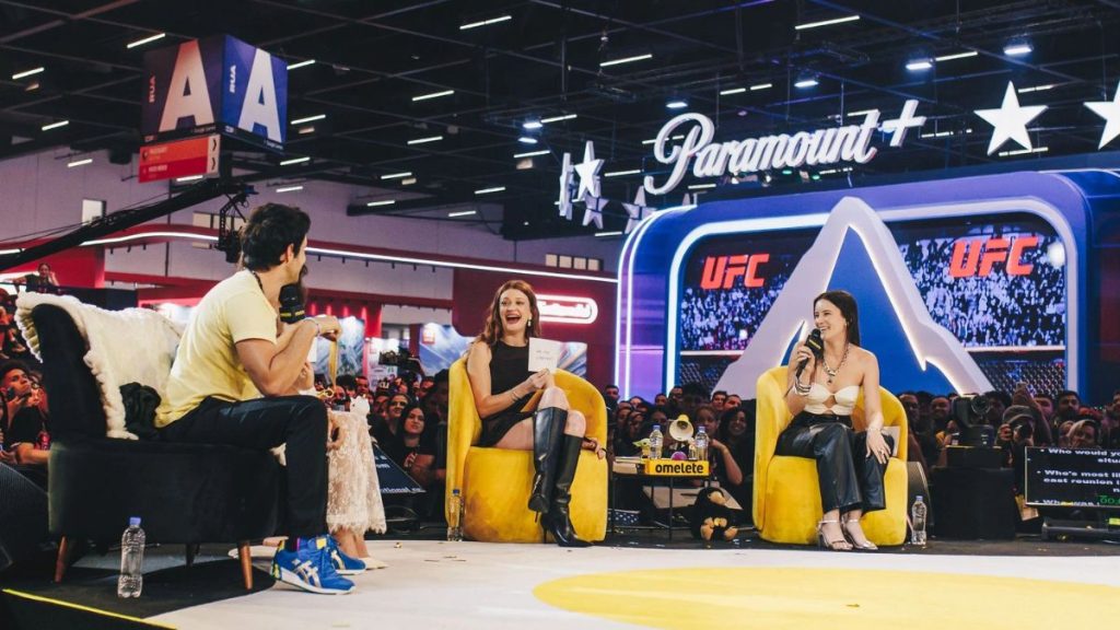 Palco da CCXP26 com apresentadores e público durante evento, em um cenário de arena com telões e marca UFC, ideal para divulgação de ingressos CCXP26