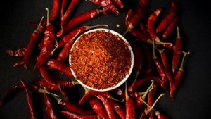Pimentas vermelhas ao redor de um recipiente com especiaria em pó, destacando tipos de pimenta e diferentes níveis de ardência para ir do suave ao explosivo.