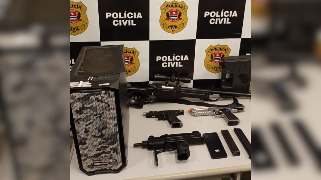 Foto da Polícia Civil com armas e simulacros apreendidos em operação: pistolas e armamento dispostos em mesa, ao lado de equipamento usado para gravações, em Santos.