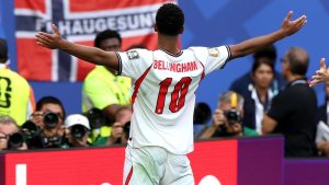 Jude Bellingham, em uniforme da Inglaterra, comemora com os braços abertos em campo durante partida após eliminação na Copa do Mundo.