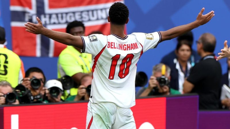 Jude Bellingham, em uniforme da Inglaterra, comemora com os braços abertos em campo durante partida após eliminação na Copa do Mundo.
