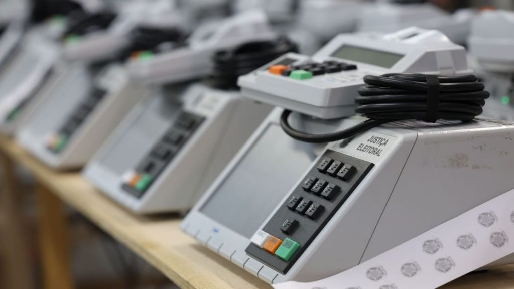 Eleições 2026: propaganda eleitoral gratuita no rádio e na TV, com close em uma central de votação eletrônica e seus botões, simbolizando a preparação para o pleito.