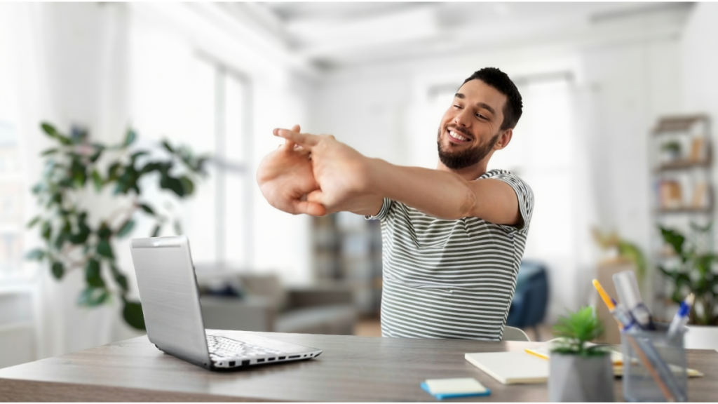 Imagem de um homem em casa, sorrindo e se alongando perto de um notebook na mesa, sugerindo dicas práticas para retomar o ritmo de trabalho com tranquilidade e foco após a Ressaca emocional pós-Copa.