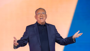 Galvão Bueno aparece em palco, de terno, com as mãos abertas em gesto de despedida, enquanto fala sobre sua participação nas Copas e o Mundial de 2030.