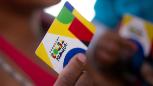 Encontro regional do Bolsa Família e Cadastro Único em Americana: mão segura cartão com logotipo do programa e cores do Brasil, em registro de evento nesta terça.
