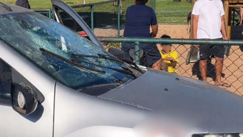 Homem preso por racismo em Paulínia: equipe policial aparece ao lado de um carro com vidro danificado após briga, enquanto pessoas observam atrás de uma cerca em área externa.
