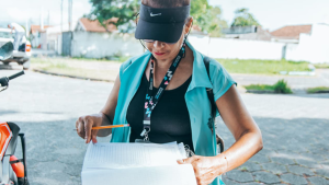 Concurso público em Itanhaém com foco em vagas para agente comunitário de saúde, ilustrado por uma profissional de saúde em atividade externa com prancheta e crachá.
