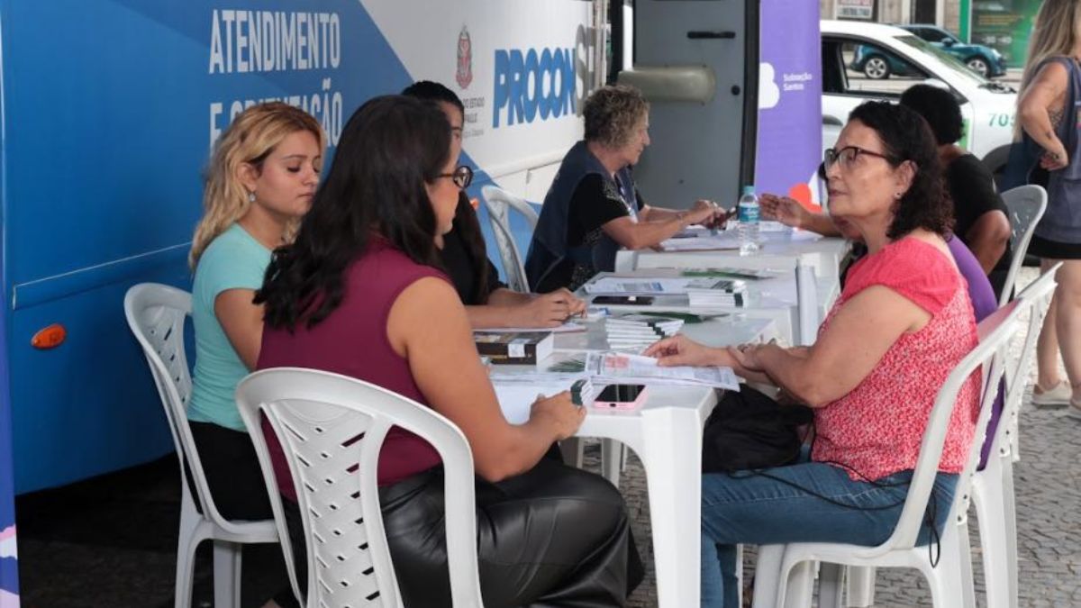 Atendimento do Procon Móvel em Santos em área externa, com equipe e moradores sentados em uma mesa durante o serviço ao público na quinta-feira.