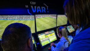 Profissionais acompanham a transmissão de futebol em telões com a marca CBF e a tecnologia VAR, em cenário que remete ao CBF Impedimento semiautomático.