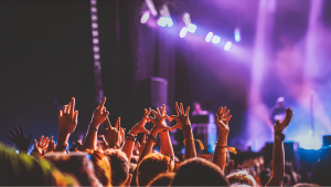 Público com mãos levantadas em um show com luzes roxas ao fundo, com destaque para orientações sobre reembolso de show cancelado pelo Procon-SP.