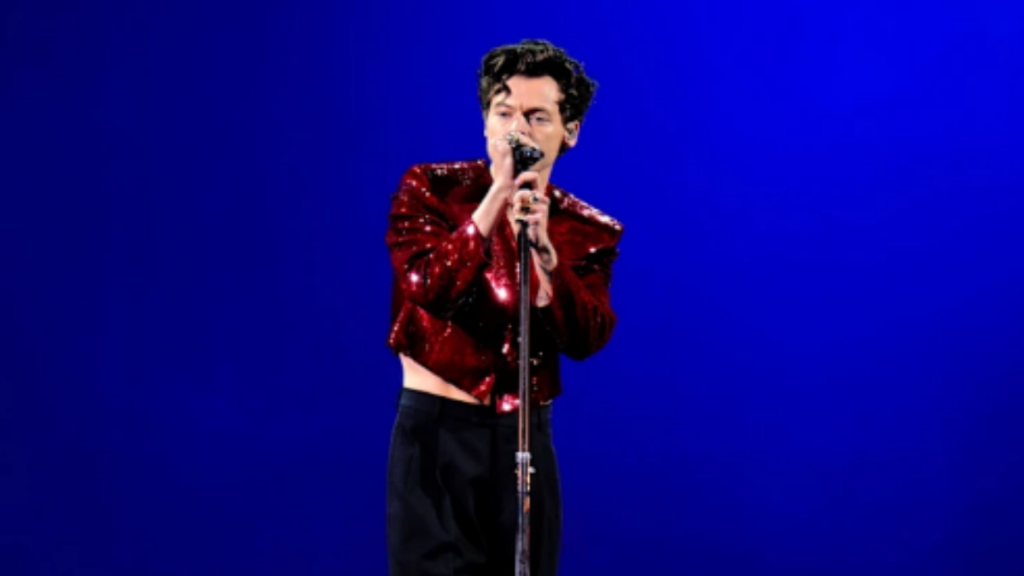 Harry Styles em apresentação ao vivo no palco, com jaqueta vermelha e microfone na mão, em imagem relacionada ao show cancelado no MorumBIS em São Paulo. reembolso de show cancelado