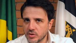 Renan Santos em entrevista, ao lado de bandeiras do Brasil e de um partido, com candidatura à Presidência confirmada pelo Missão