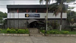 CrianÃ§as resgatadas em guarujÃ¡: fachada da PolÃ­cia Delegacia de PolÃ­cia de GuarujÃ¡, no litoral de SP, onde casos de ferimentos e investigaÃ§Ã£o da mÃ£e sÃ£o registrados, com prÃ©dio e jardim ao redor.