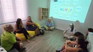 Encontro em sala com participantes sentados em círculo durante o Workshop para responsáveis atípicos, em Praia Grande, nesta quarta, com apresentação em telão ao fundo.
