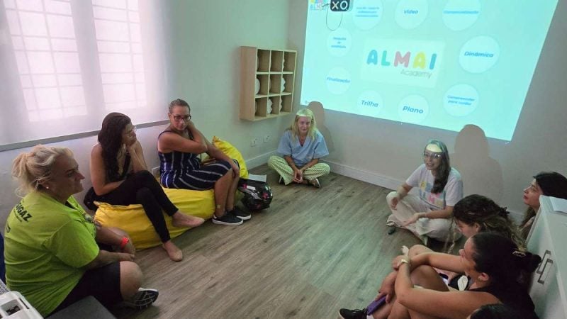 Encontro em sala com participantes sentados em círculo durante o Workshop para responsáveis atípicos, em Praia Grande, nesta quarta, com apresentação em telão ao fundo.