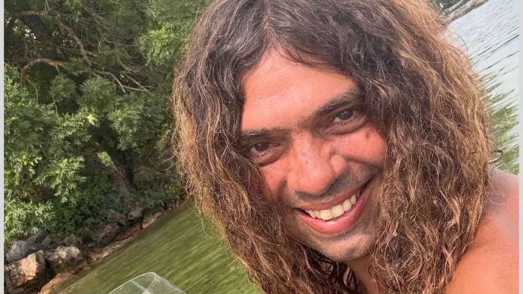 Retrato em close de um homem com cabelo cacheado e barba, sorrindo em foto na natureza à beira de um lago, em contexto de notícia sobre morte no Lago Léman. jornalista Francisco de Assis