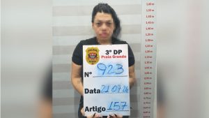 Mulher detida pela PolÃ­cia Civil em Pria Grande (3Âº DP), no litoral de SP, segurando cartaz de identificaÃ§Ã£o com data e artigo, suspeita de golpe boa noite cinderela contra idoso.