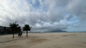 ventos fortes na Baixada: praia com céu nublado, ondas e areia ao longo da orla, com ventania visível afetando travessias e operações no Porto de Santos
