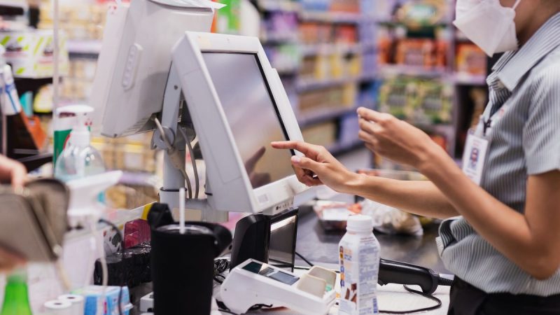 Trabalhador no comércio usando caixa registradora em loja, durante trabalho em feriados e atendimento ao cliente.