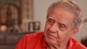 Retrato do cineasta Luiz Carlos Barreto em imagem de estúdio, com cabelos grisalhos e expressão serena, em destaque contra fundo desfocado de interior. Notícia de morte aos 98 anos no Rio de Janeiro.