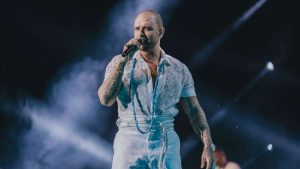 Diogo Nogueira faz show no palco ao microfone, com fumaça e luzes ao fundo, em um evento relacionado à Festa dos Pais em Hortolândia, com apresentação gratuita.