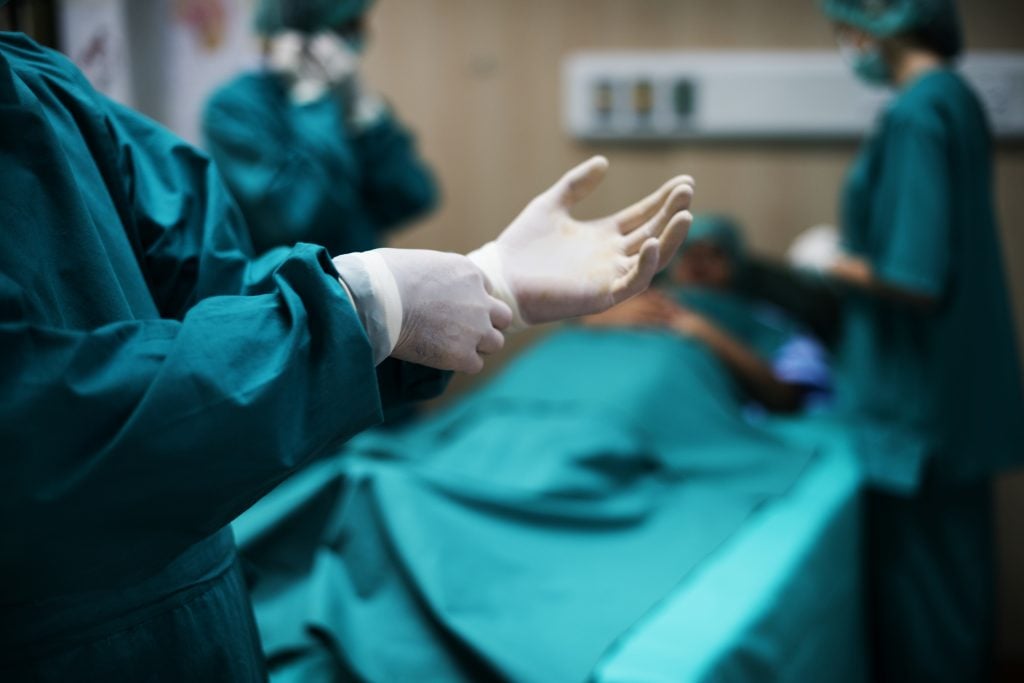 Equipe médica em sala cirúrgica, com profissionais usando batas e luvas, braços apontados e campo cirúrgico ao fundo, representando Cirurgias oncológicas Piracicaba em hospitais do SUS