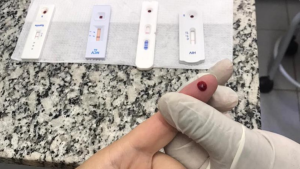 testes rápidos de ISTs Americana: Mão com luva manipulando um cassette de teste rápido de ISTs e HIV em ação gratuita da Americana com prevenção às ISTs, ambiente clínico e kits sobre bancada de granito.