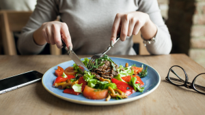 Pessoa servindo salada em prato azul, com legumes e verduras, enquanto observa-se alimentaÃ§Ã£o saudÃ¡vel em ambiente interno; tema relacionado ao mapa da fome ONU.