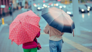 Frente fria avança por SP e MS, derruba temperaturas e traz chuva forte: pessoas com guarda-chuvas caminham na rua em dia nublado e chuvoso.