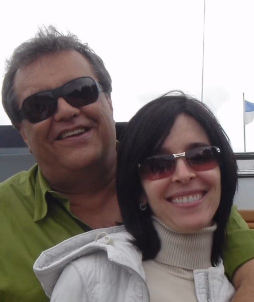 Dennis Carvalho e Deborah posam sorrindo em uma foto juntos, em ambiente externo, com óculos de sol e roupas casuais, celebrando o casamento de 24 anos.