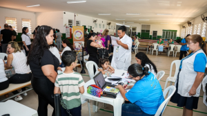 Equipe de saúde em sala de atendimento durante o fim de semana, com vacinação e serviços gratuitos em cidades da região, enquanto cidadãos e crianças recebem orientações.