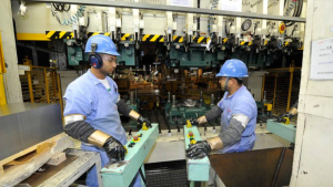 nova taxa Estados Unidos: Trabalhadores em linha de produção industrial com máquinas ao fundo, enquanto os Estados Unidos ampliam tarifas sobre produtos brasileiros com nova taxa de 12,5%.
