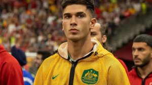 Cristian Volpato, jogador em partida na Austrália, aparece em foto no estádio usando agasalho amarelo com escudo do país. Matéria cita teste positivo para cocaína.