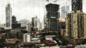 Previsão do tempo em São Paulo: janela com chuva e gotas no vidro sobre prédios ao fundo, indicando chuva e queda nas temperaturas neste fim de semana.