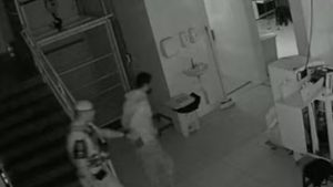 Câmera de segurança em uma fábrica durante invasão em fábrica de Campinas, com suspeito sendo abordado e objetos espalhados em área interna ao fundo.