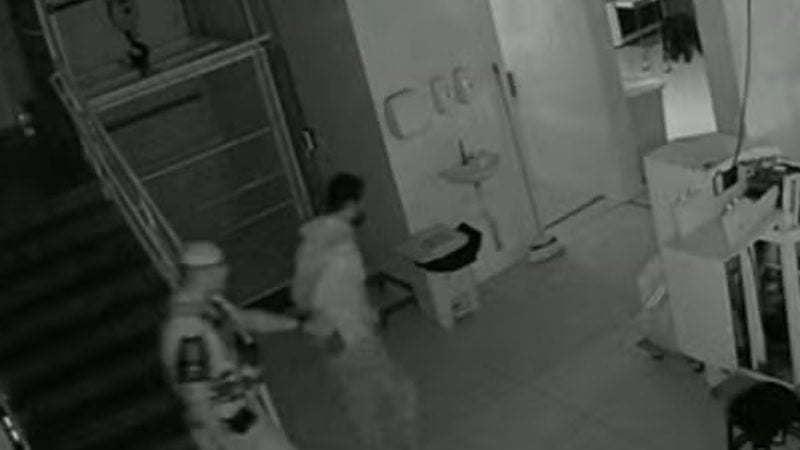 Câmera de segurança em uma fábrica durante invasão em fábrica de Campinas, com suspeito sendo abordado e objetos espalhados em área interna ao fundo.
