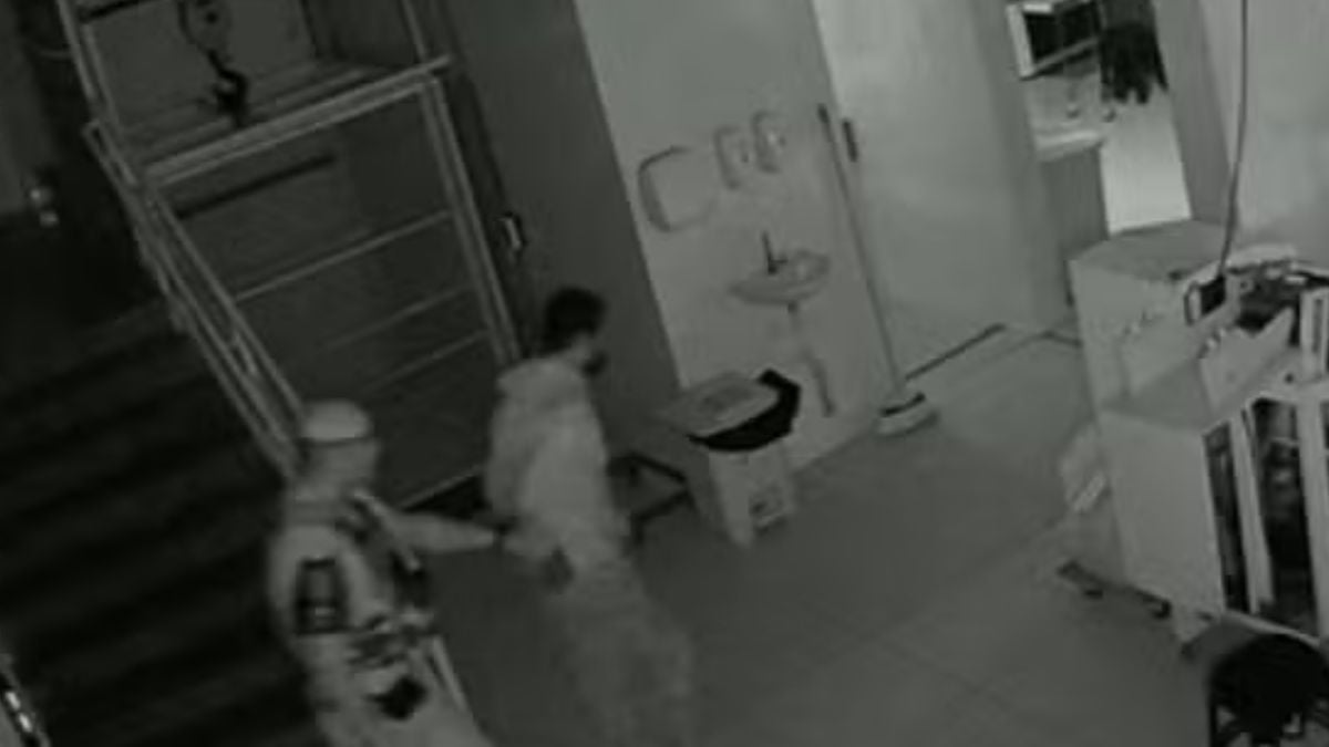 Câmera de segurança em uma fábrica durante invasão em fábrica de Campinas, com suspeito sendo abordado e objetos espalhados em área interna ao fundo.