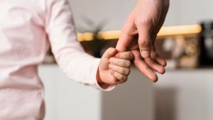 mutirão paternidade Americana: Americana recebe mutirão de reconhecimento e investigação de paternidade, com uma mão adulta segurando o dedo de uma criança, simbolizando o apoio e a busca pela paternidade