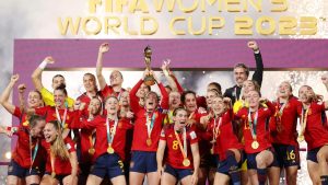 Equipe feminina comemora com troféu e medalhas após vitória, em cenário de premiação; Fifa abre cadastro de interesse para voluntários da Copa do Mundo Feminina.