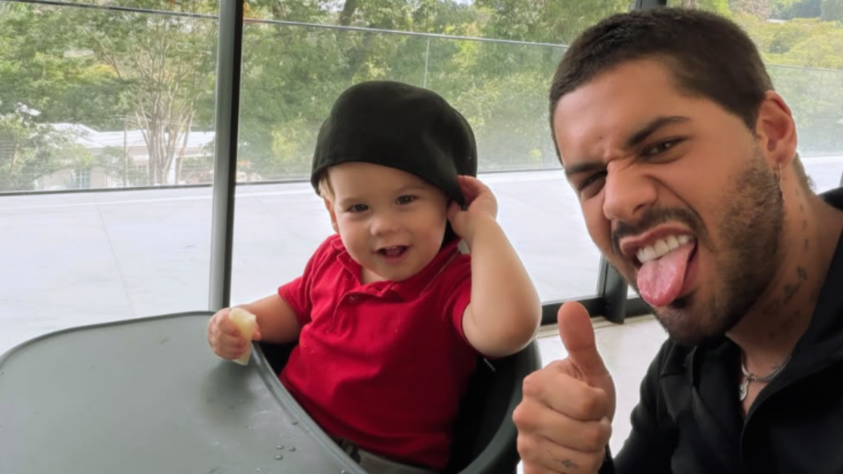 Zé Felipe pede desculpas: Zé Felipe aparece sorrindo ao lado de um bebê em ambiente interno, com expressão de pedido de desculpas após polêmica em vídeo com o filho, em foto de declaração.